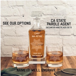 May include: A set of two clear glass tumblers and a clear glass decanter with a star-shaped design and the text "CA State Parole Agent" and "Chief Ima Retire". The decanter and glasses are engraved with a star-shaped design and the text "State Parole Agent" and "California 3730".