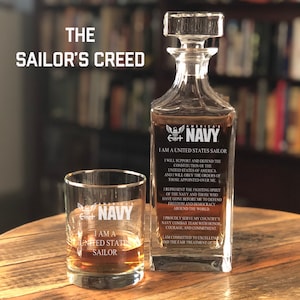 K&ouml;nnte beinhalten: Eine klare Glaskaraffe mit einer dunkelblauen Inschrift, die "America's Navy" und "I am a United States Sailor" lautet. Die Karaffe ist mit einer klaren Fl&uuml;ssigkeit gef&uuml;llt. Ein klares Glas mit einer dunkelblauen Inschrift, die "I am a United States Sailor" lautet, steht neben der Karaffe. Die Inschrift auf beiden Gl&auml;sern enth&auml;lt den Text "America's Navy".