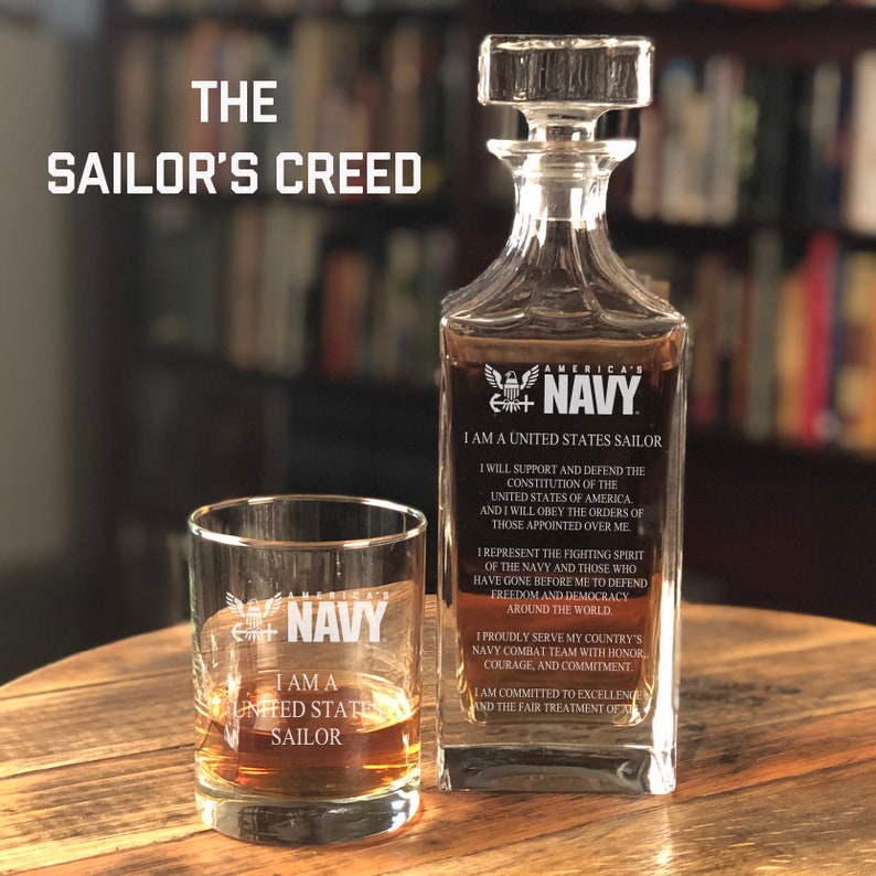 K&ouml;nnte beinhalten: Eine klare Glaskaraffe mit einer dunkelblauen Inschrift, die "America's Navy" und "I am a United States Sailor" lautet. Die Karaffe ist mit einer klaren Fl&uuml;ssigkeit gef&uuml;llt. Ein klares Glas mit einer dunkelblauen Inschrift, die "I am a United States Sailor" lautet, steht neben der Karaffe. Die Inschrift auf beiden Gl&auml;sern enth&auml;lt den Text "America's Navy".