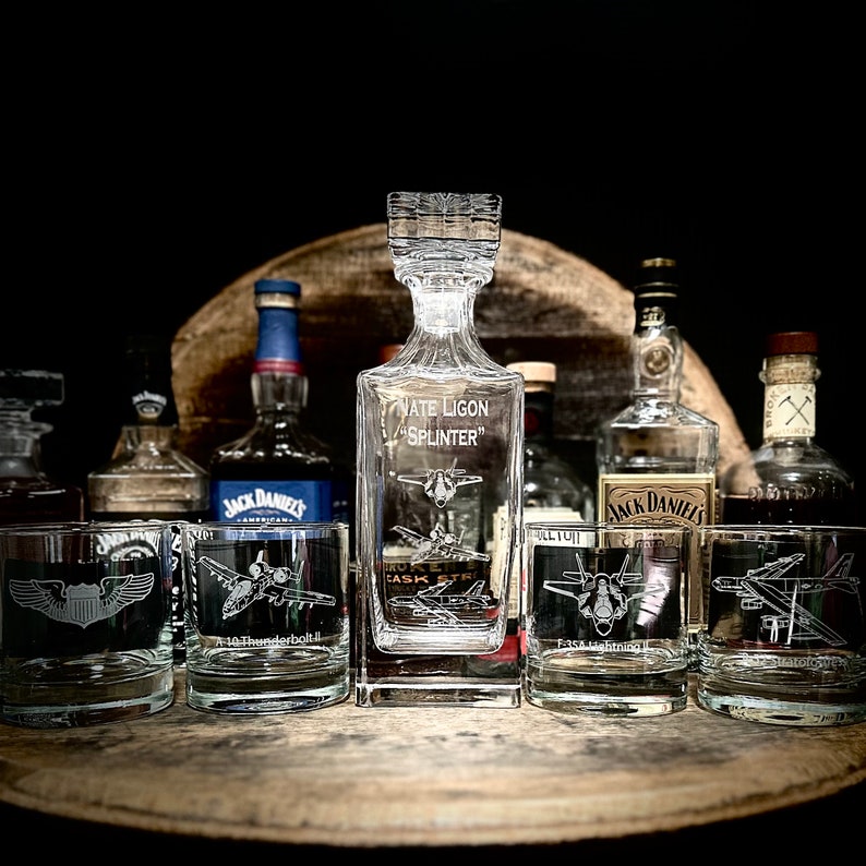 May include: A collection of clear glass decanters and glasses with etched designs of military aircraft. The decanter is engraved with the text "Nate Ligon "Splinter"".