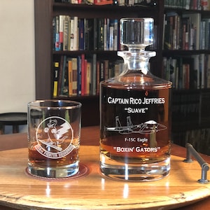 May include: A personalized glass decanter with a clear glass design and a stopper. The decanter is engraved with the text "Captain Rico Jeffries "Suave" F-15C Eagle "Boxin' Gators".