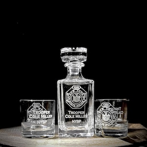 May include: A set of three clear glass decanters with etched designs. The decanters feature the New York State Police logo and the text "Trooper Cole Miller NYSP".
