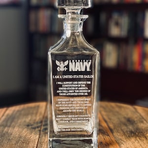 K&ouml;nnte beinhalten: Eine klare Glaskaraffe mit einem Stopfen und einem ge&auml;tzten Design der amerikanischen Flagge und den Worten "America's Navy". Die Karaffe tr&auml;gt ein Zitat, das auf der Seite einge&auml;tzt ist und lautet: "Ich bin ein Seemann der Vereinigten Staaten... Ich werde die Verfassung der Vereinigten Staaten von Amerika unterst&uuml;tzen und verteidigen... Ich werde den Befehlen derer gehorchen, die &uuml;ber mir stehen... Ich repr&auml;sentiere den k&auml;mpferischen Geist der Marine und derer, die vor mir gegangen sind, um Freiheit und Demokratie in der ganzen Welt zu verteidigen... Ich diene mit Stolz im Kampfteam der Marine meines Landes mit Ehre, Mut und Engagement... Ich bin verpflichtet, die h&ouml;chsten Verhaltensstandards und die faire Behandlung aller zu wahren."