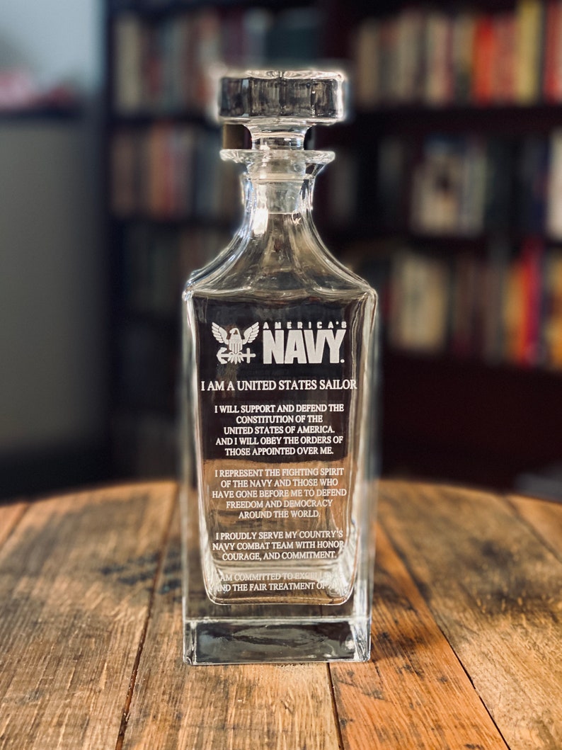 K&ouml;nnte beinhalten: Eine klare Glaskaraffe mit einem Stopfen und einem ge&auml;tzten Design der amerikanischen Flagge und den Worten "America's Navy". Die Karaffe tr&auml;gt ein Zitat, das auf der Seite einge&auml;tzt ist und lautet: "Ich bin ein Seemann der Vereinigten Staaten... Ich werde die Verfassung der Vereinigten Staaten von Amerika unterst&uuml;tzen und verteidigen... Ich werde den Befehlen derer gehorchen, die &uuml;ber mir stehen... Ich repr&auml;sentiere den k&auml;mpferischen Geist der Marine und derer, die vor mir gegangen sind, um Freiheit und Demokratie in der ganzen Welt zu verteidigen... Ich diene mit Stolz im Kampfteam der Marine meines Landes mit Ehre, Mut und Engagement... Ich bin verpflichtet, die h&ouml;chsten Verhaltensstandards und die faire Behandlung aller zu wahren."