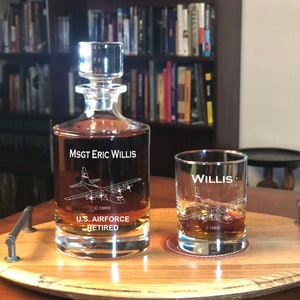 May include: A personalized decanter and glass set with a C-130H3 aircraft design. The decanter is engraved with "MSGT Eric Willis, U.S. AIRFORCE RETIRED". The glass is engraved with "WILLIS" and a C-130H3 aircraft design.