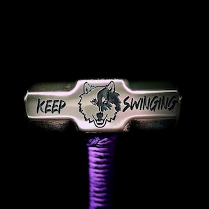 May include: A silver hammer with a wolf head design and the words "Keep Swinging" engraved on it. The hammer has a purple rope handle.
