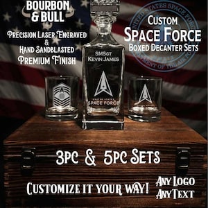 May include: A clear glass decanter and two matching glasses featuring laser-engraved United States Space Force logos and the text SMSGT KEVIN JAMES. The set is displayed on a dark wooden box with metal latches, with text reading BOURBON & BULL, CUSTOM SPACE FORCE BOXED DECANTER SETS, 3PC & 5PC SETS, and CUSTOMIZE IT YOUR WAY.