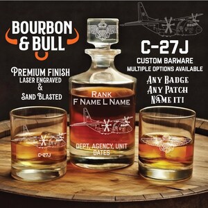 May include: A custom barware set featuring a decanter and two glasses, laser engraved with a C-27J aircraft design. The decanter has a glass stopper with a crest. Text includes "Bourbon & Bull" and "Premium Finish".