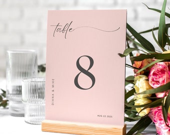 May include: Pink table number card with the number 8 printed in black. The card is on a wooden stand and says "Table" in cursive at the top. The text "Diana & Mike" is printed on the left side of the card and "Aug 22 2025" is printed at the bottom.