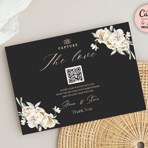 以下が含まれることがあります： 白い花とQRコードが付いた黒い結婚式フォトブースのサイン。サインには「Capture the love」と「Anna & Steve」と「Thank You」の文字が書かれています。
