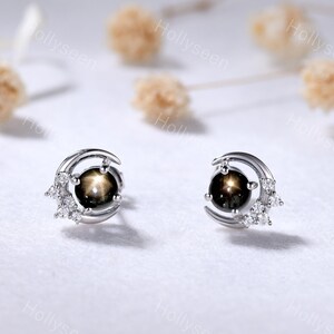 May include: A pair of silver earrings with a crescent moon design and a black star-shaped gemstone in the center. The earrings are accented with small white gemstones.