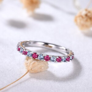 May include: A delicate silver band ring with alternating blue and pink gemstones. The ring is set on a white background.