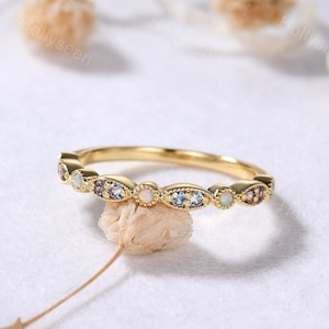 May include: A delicate gold band ring with a row of oval-shaped opal and light blue gemstones. The ring has a vintage-inspired design.
