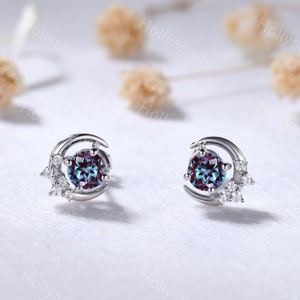 May include: A pair of silver crescent moon earrings with a blue gemstone in the center and small clear gemstones around the moon.