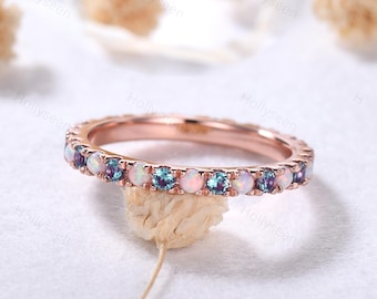 May include: A rose gold band ring with a delicate row of alternating opal and blue gemstones.
