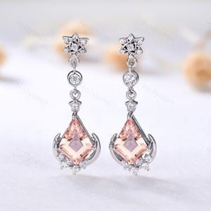 May include: A pair of silver dangle earrings with a star-shaped top and a large, square-shaped pink gemstone. The earrings are accented with smaller clear gemstones.