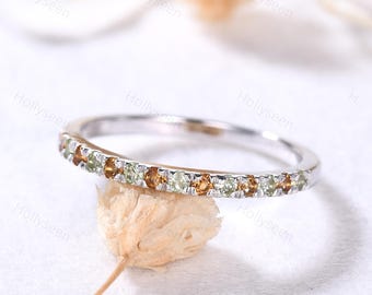 May include: A delicate silver band ring with a row of small, round, green and orange gemstones.