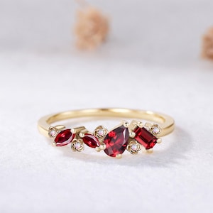 May include: A gold ring featuring a cluster of red garnet gemstones in pear, marquise, and baguette cuts, accented by small round white opals set within delicate gold flower-shaped metal settings along the thin, polished gold band.