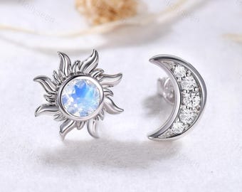 Può includere: Un paio di orecchini d'argento con un design a forma di sole e luna. L'orecchino a forma di sole ha un centro rotondo in pietra di luna e l'orecchino a forma di luna è decorato con piccoli zirconi cubici trasparenti.