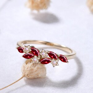 May include: A gold ring featuring a cluster of marquise-cut red gemstones and small star-shaped accents, each set with a tiny iridescent stone. The band is thin and polished, showcasing a delicate arrangement of these vibrant red marquise stones.