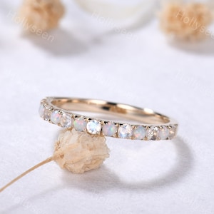 May include: A delicate gold band ring with a row of small, round, white opal gemstones. The ring is set on a white background.