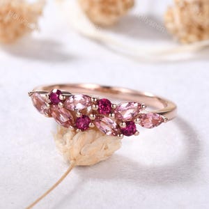 May include: A delicate rose gold ring with a cluster of pink and red gemstones set in a leaf-like design.