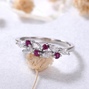May include: A delicate silver ring with a floral design featuring marquise-shaped diamonds and small ruby accents.