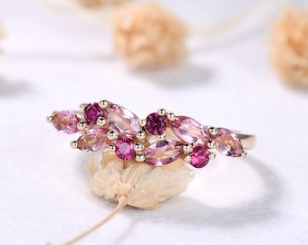 Può includere: Un anello d'oro con un design floreale con pietre preziose rosa e magenta. L'anello presenta pietre preziose taglio marquise e rotonde, creando un insieme colorato. Le pietre sono incastonate in una fascia d'oro.