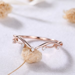 May include: A delicate rose gold ring with a V-shaped design and small diamonds set along the band.