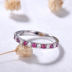 May include: A delicate silver band ring with alternating pink and white gemstones. The ring is set with small round stones.