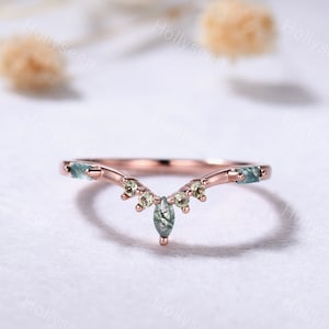 May include: A delicate rose gold wedding band with a v-shaped design. The band is adorned with small green and yellow gemstones.