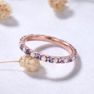 Könnte beinhalten: Ein Roségold-Bandring mit einer zarten Reihe abwechselnder weißer Opal- und lila Amethyst-Edelsteine.