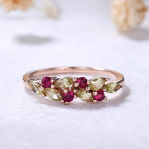 May include: A rose gold ring featuring a cluster of marquise-cut light green stones and round-cut vibrant pink stones arranged in a leaf-like pattern along the band. The metal band has a smooth, polished finish and a warm, metallic pink hue.