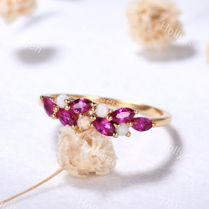 May include: A delicate gold band ring with a cluster of pink marquise-shaped gemstones and white round gemstones. The ring is set against a white background.