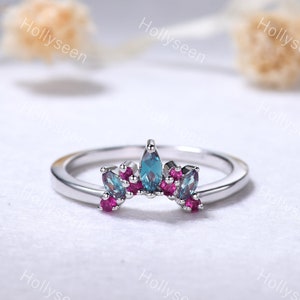 May include: A silver ring with a crown-shaped design featuring blue and pink gemstones. The ring is set on a white background.