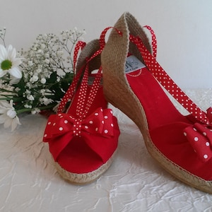 Op de afbeelding: Rode espadrilles met plateauzool, witte stippen en een rode strik. De schoenen hebben een jute zool en een wit gestippeld lint.