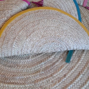 May include: A half-circle straw clutch with a yellow trim and a brown leather strap. The clutch is made of woven straw and has a teal blue leather strap.