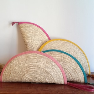 May include: Three half-circle straw clutches with different colored leather trim. The clutches are pink, yellow, and teal.