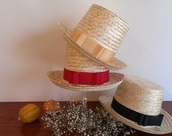 May include: Three straw boater hats with flat crowns and wide brims. One hat features a beige ribbon, one has a vibrant red ribbon with a bow, and the third hat is adorned with a solid black ribbon. The hats are arranged in a stacked display.