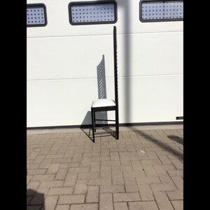 May include: A black metal chair with a white cushioned seat. The chair has a tall, open back with a geometric design.