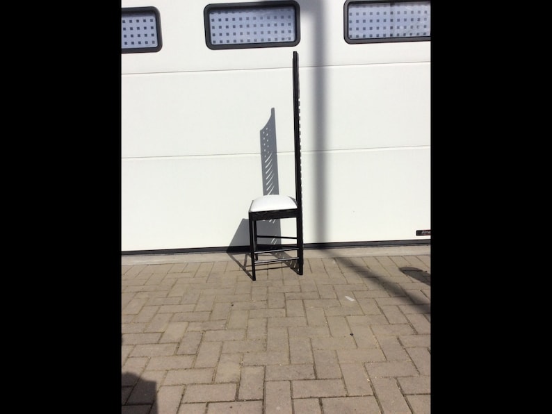 May include: A black metal chair with a white cushioned seat. The chair has a tall, open back with a geometric design.