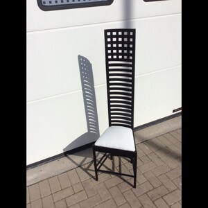 May include: A black wooden chair with a white cushion. The chair has a tall back with a geometric pattern.