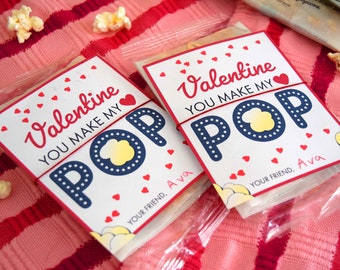 May include: Two Valentine's Day cards with popcorn and the text "Valentine You Make My Pop" with red hearts and a blue and white popcorn design. The cards are tied with red string and have the name "Ava" written on them.