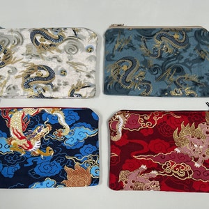 May include: Four rectangular zipped pouches featuring fabric with dragon and cloud motifs. The top left pouch is cream, the top right is blue-grey, the bottom left is dark blue with a red zip, and the bottom right is deep red with a black zip.