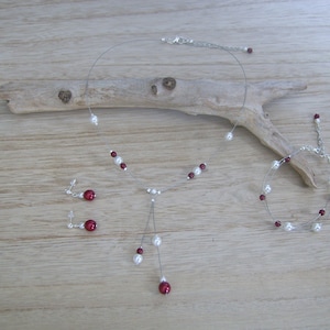 Peut inclure: Un ensemble de bijoux composé d'un collier argenté avec des perles blanches et des perles bordeaux, d'un bracelet assorti et d'une paire de boucles d'oreilles.