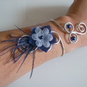 Peut inclure: Un bracelet en fil d'argent avec une fleur bleue et un embellissement en plumes. Le bracelet a trois perles bleues.