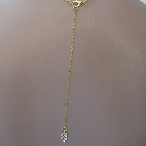 Peut inclure: Un collier en chaîne dorée avec un petit pendentif en forme de feuille à l'extrémité. La chaîne est longue et pend au dos du cou.