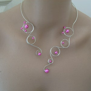 Può includere: Un girocollo in filo d'argento con un design delicato e asimmetrico. Il girocollo presenta perline rosa e una forma organica fluida.