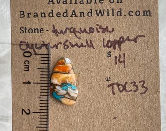 May include: A close-up of a turquoise and copper cabochon stone, measuring approximately 1.5 inches in length. The stone has a variety of colors, including turquoise, copper, orange, and white. The stone is labeled "turquoise" and "eysturshell copper" and is priced at $14. The stone is available on BrandedAndWild.com with the item number #TOC33.