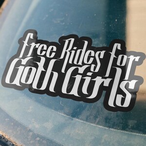 Puede incluir: Una pegatina de vinilo negro aplicada en la ventana de un coche con el texto blanco "Free Rides for Goth Girls" escrito en una fuente estilizada de inspiración gótica. La pegatina tiene un aspecto audaz y de alto contraste sobre el cristal.
